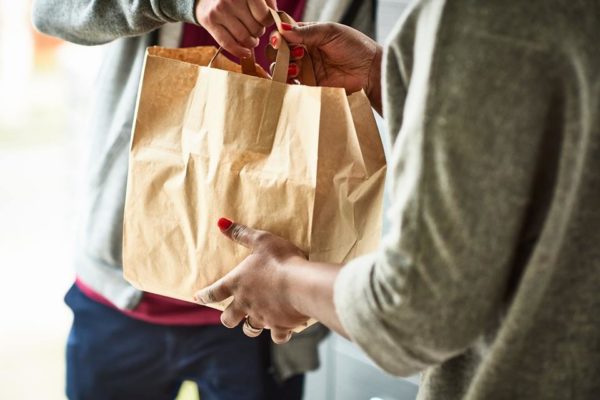 Na foto, mulher recebendo entrega de comida para viagem em sacola de papel - Metrópoles