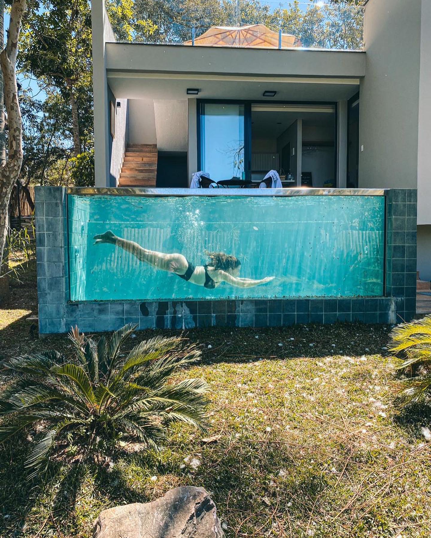 Foto colorida. Imagem foca na piscina de borda infinita. Pela imagem dá para ver uma mulher dentro da piscina com borda transparente - Metrópoles