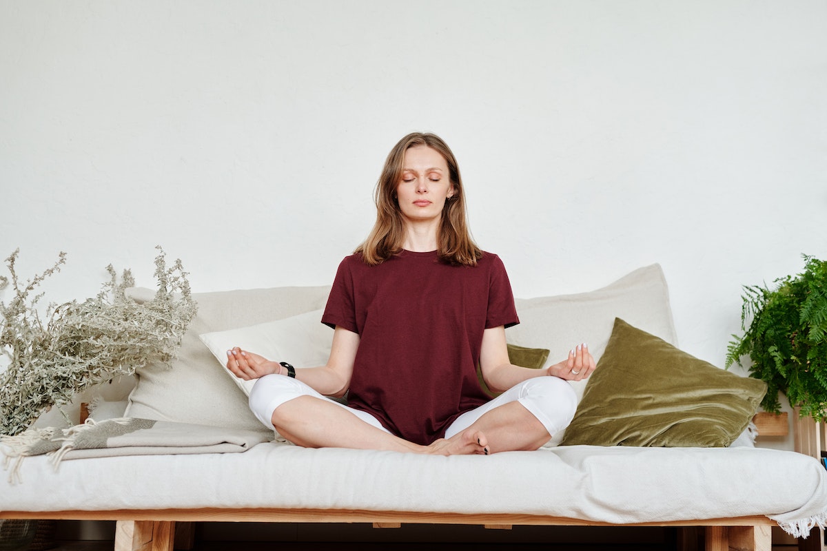 Mulher jovem realizando meditação em sofá de casa - Metrópoles