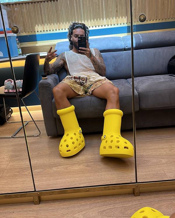 Maluma tira selfie sentado em sofá usando bota amarela gigante - Metrópoles