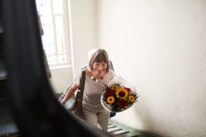 Foto mostra mulher idosa subindo uma escada com um ramo de flores - Metrópoles