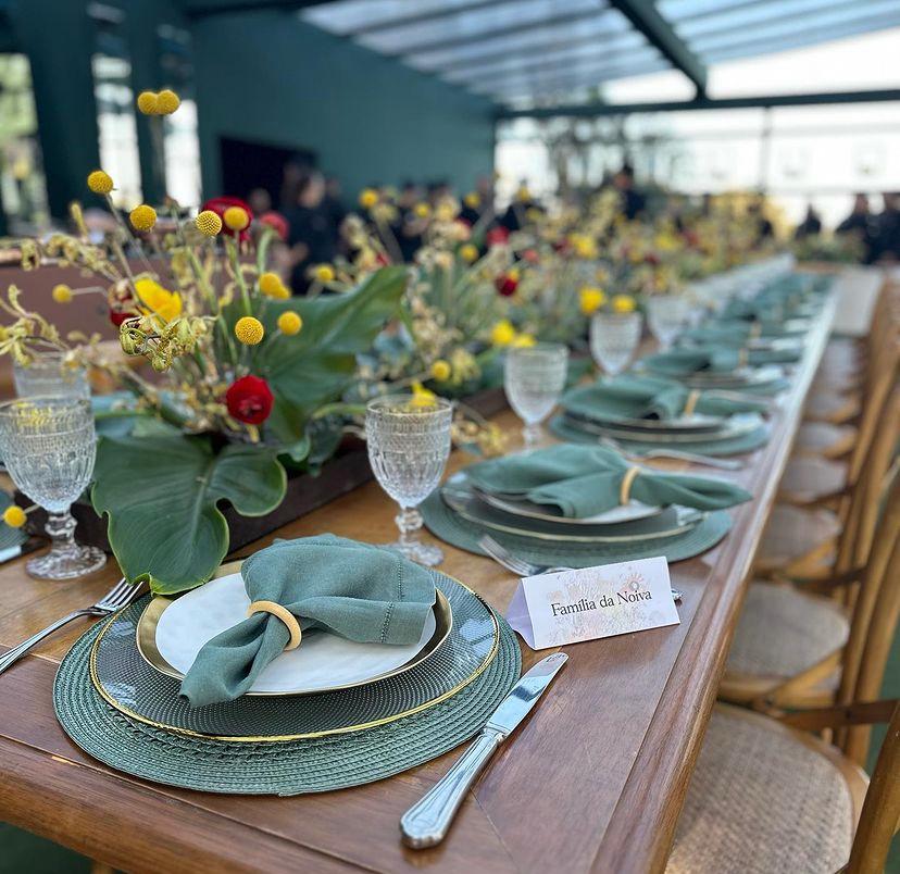 Mesa de almoço com utensílios verdes e flores no centro - Metrópoles