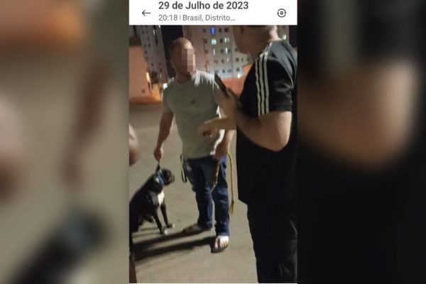 Print colorido de um homem segurando um cachorro enquanto olha para outro homem na frente dele - Metrópoles