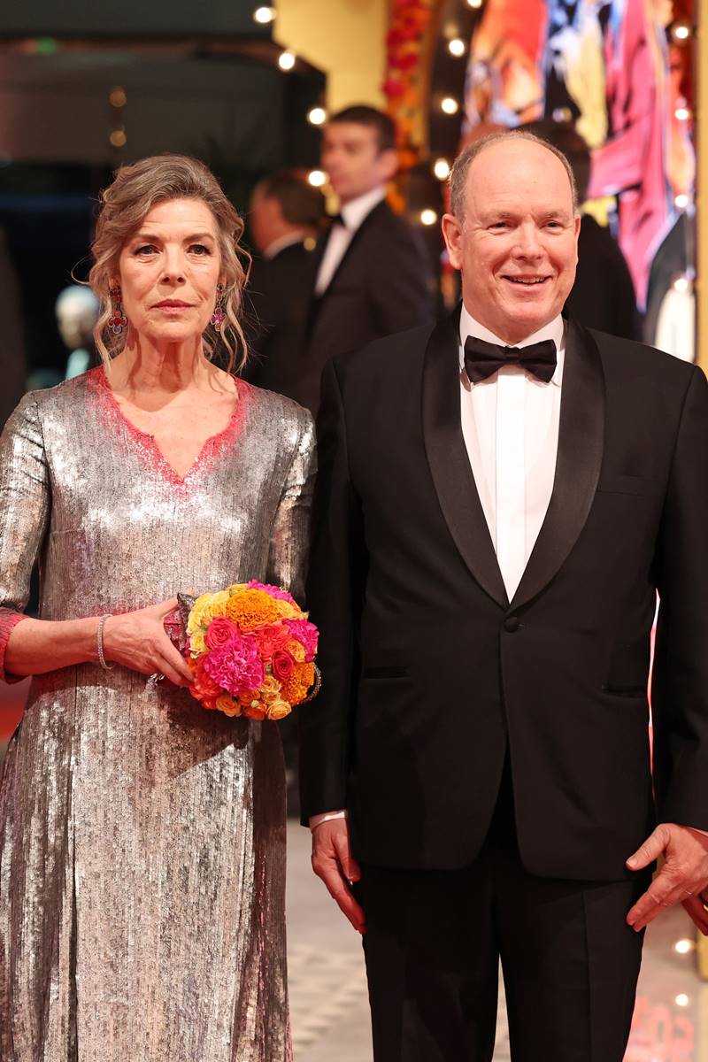 Foto colorida de mulher, branca, loira e madura, com vestido prateado e segurando um buquê. Ela está ao lado de um homem, branco e calvo, com terno - Metrópoles 