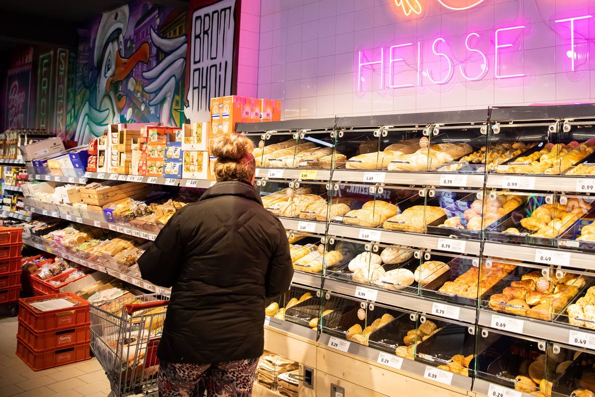 Foto colorida de mulher ruiva olhando pães em uma prateleira de um supermercado - Metrópoles