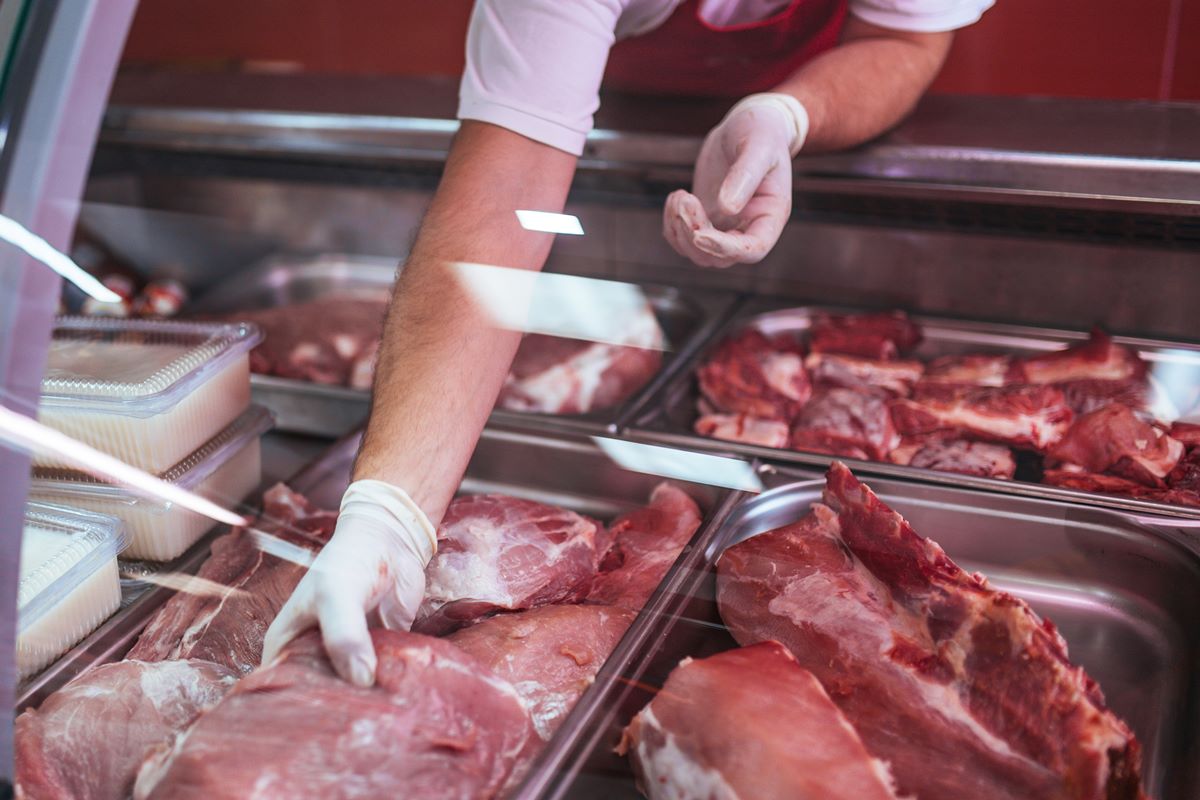 Foto colorida de mão masculina, com luvas, pegando carne dentro de freezer - Metrópoles