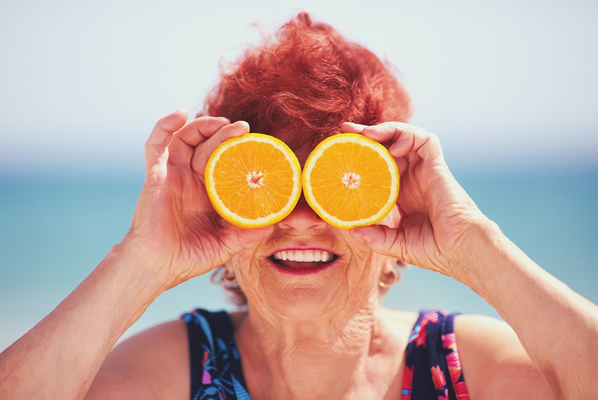 Mulher idosa de cabelo ruivo segurando duas fatias de laranja cortadas nos olhos - Metrópoles