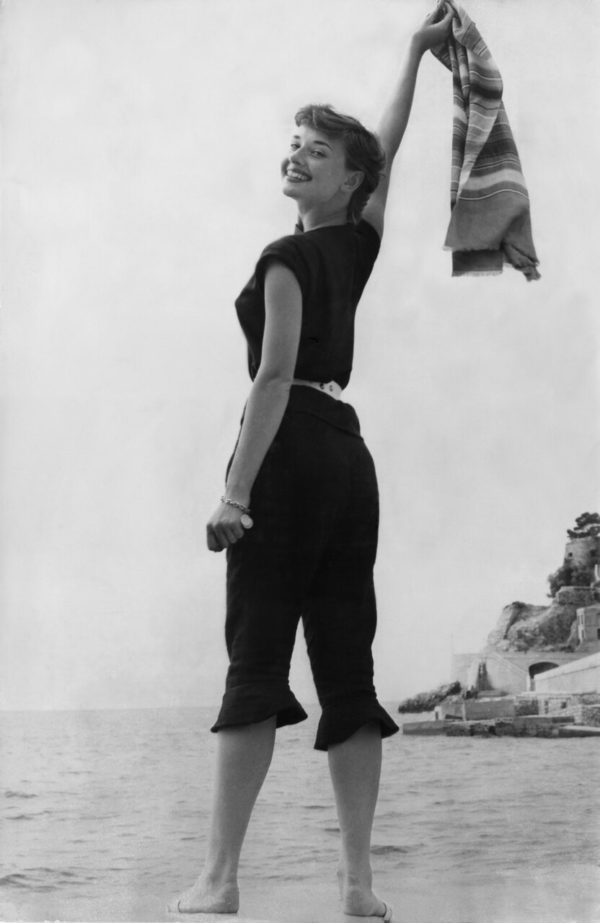 Na imagem com cor, Audrey Hepburn na praia usando calça capri - Metrópoles