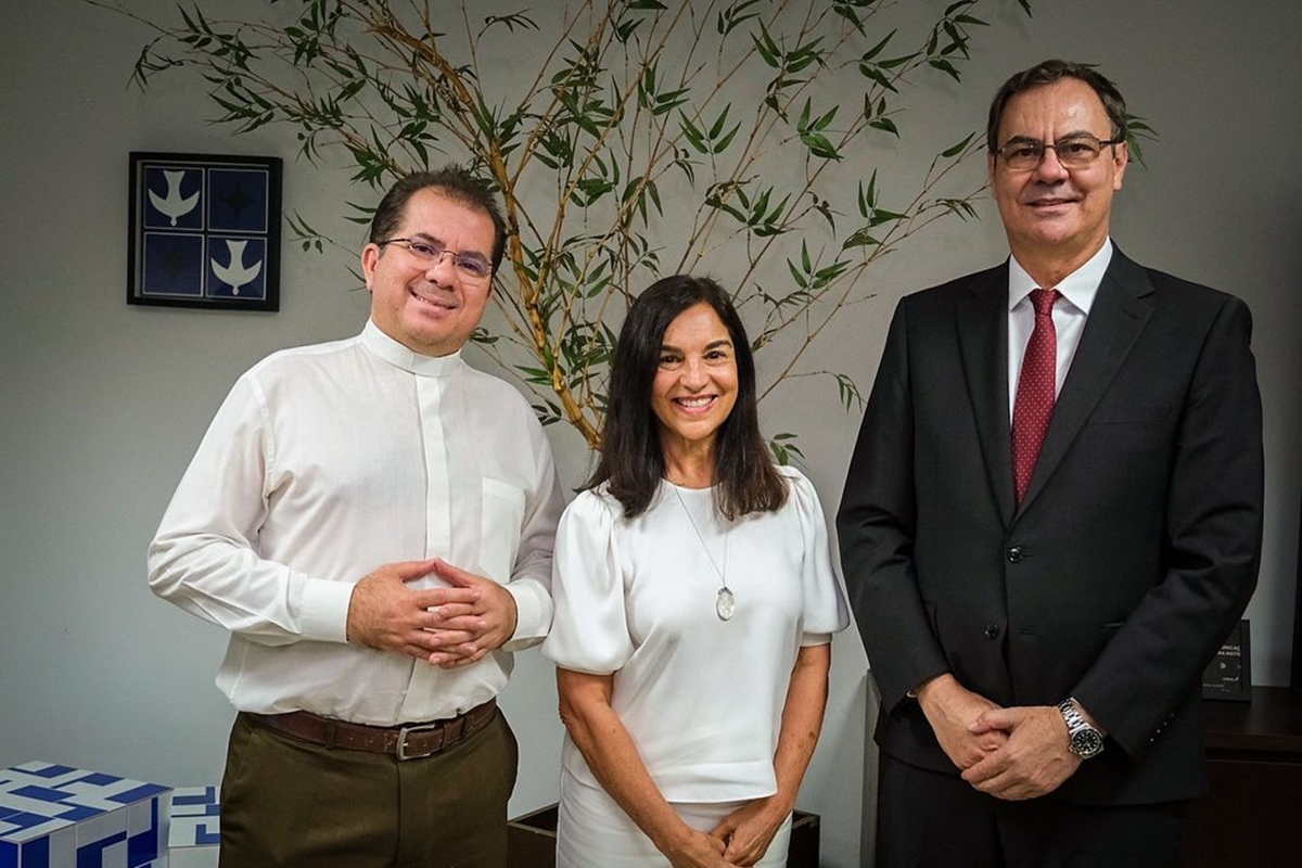 Foto colorida de três pessoas, sendo uma mulher parda e com roupas brancas entre dois homens, um deles usa uma blusa branca e o outro um terno - Metrópoles