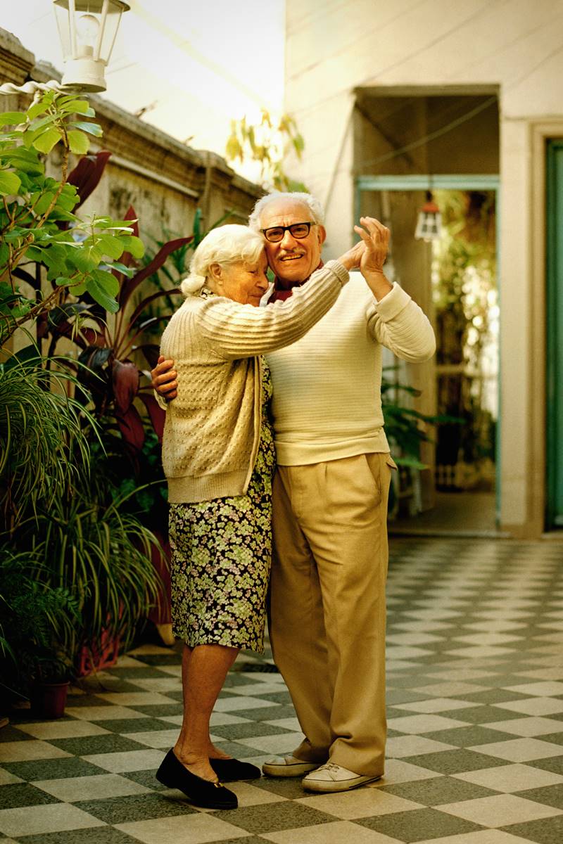 Foto colorida de casal idoso dançando abraçados. No espaço, há um jardim vertical - Metrópoles