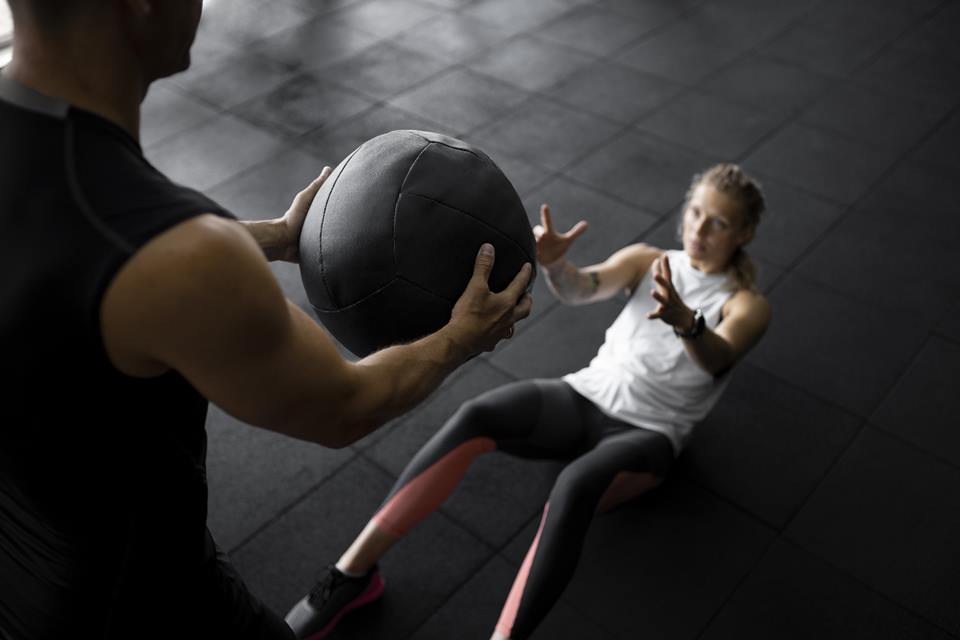 Foto colorida de mulher sendo ajudada por um personal trainer na academia - Metrópoles 