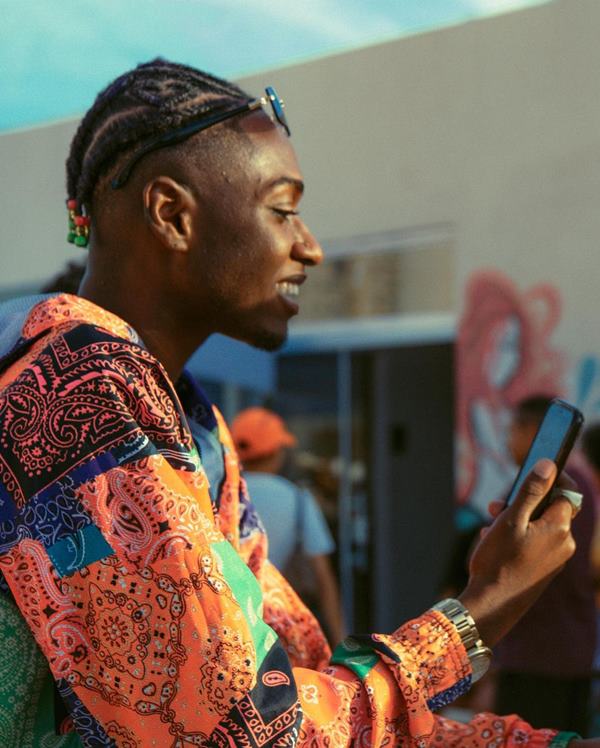 Homem preto com casaco colorido usando o celular - Metrópoles