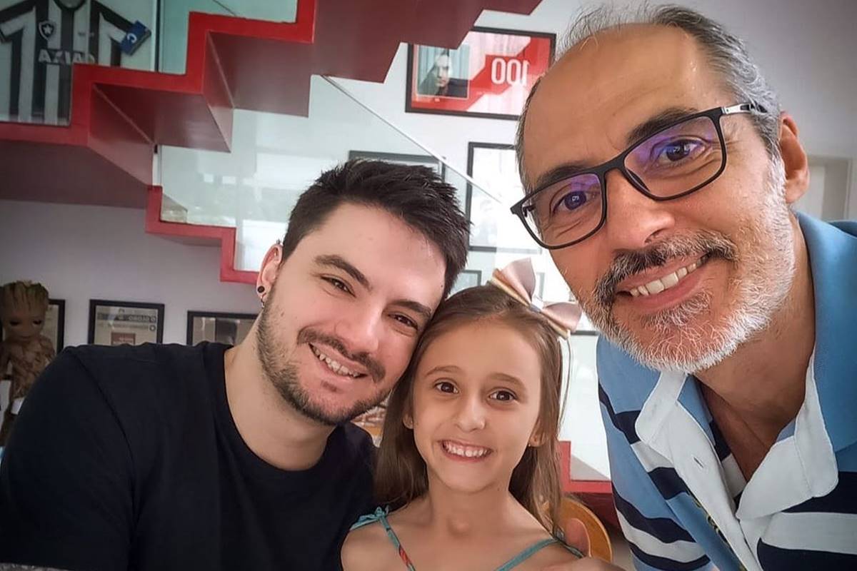 felipe neto posa de camiseta preta ao lado de uma menina com laço na cabeça e um homem de meia idade com camiseta polo listrada em tons de azul e branco e óculos de grau - metrópoles