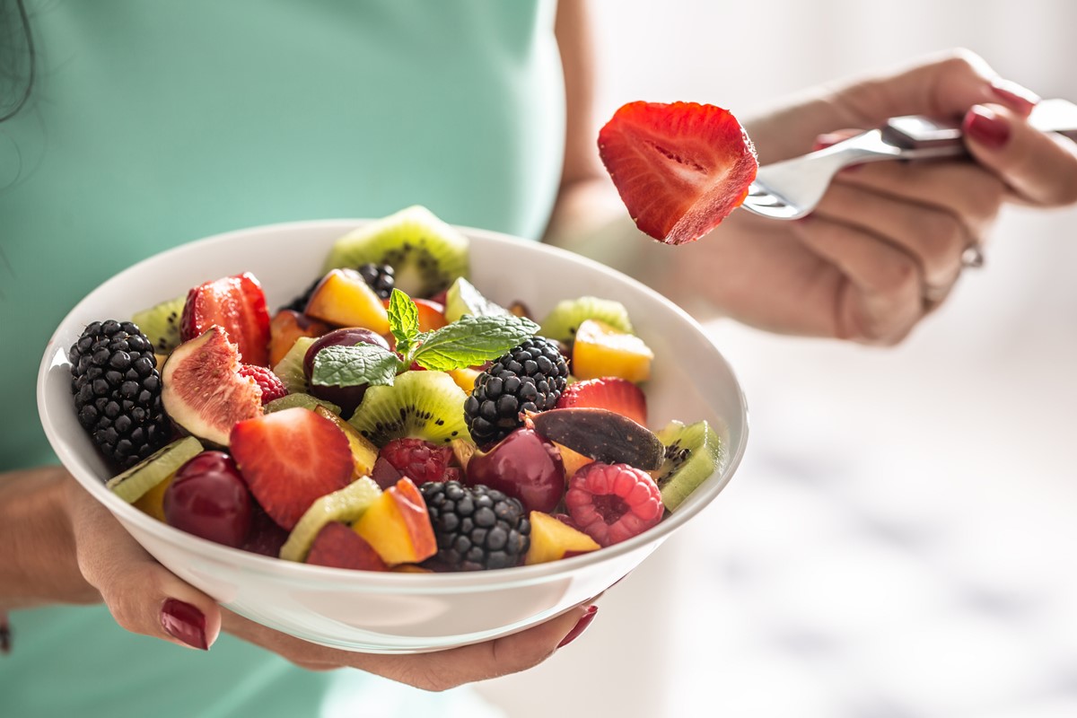 Foto colorida de tigela branca com variedade de frutas. Tem morango dividido ao meio em um garfo - Metrópoles