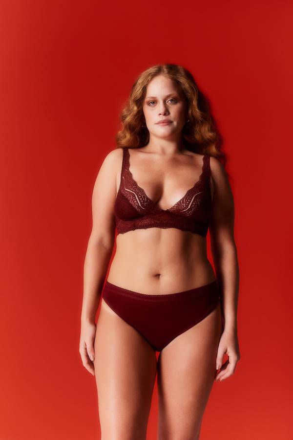 Em fundo vermelho, mulher usa conjunto vinho de lingeries com calcinha e sutiã - Metrópoles