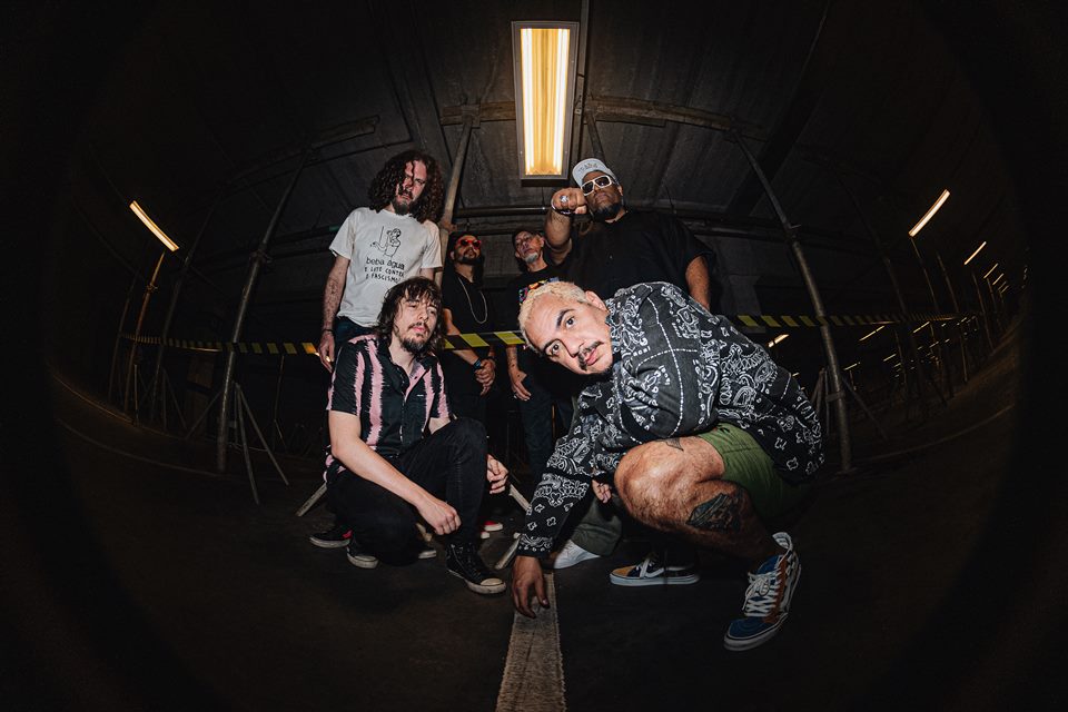 Foto do grupo Planet Hemp. Seis homens posam para uma foto em local escuro. Dois estão agachados na frente e quatro em pé atrás - Metrópoles