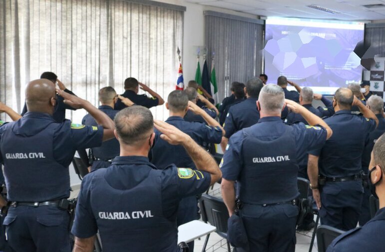 Em foto colorida GCMs de costas batem continência dentro de sala - Metrópoles 