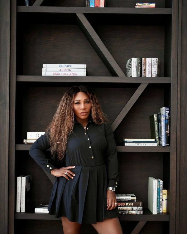 Mulher com vestido preto posando em frente a uma estante de livros