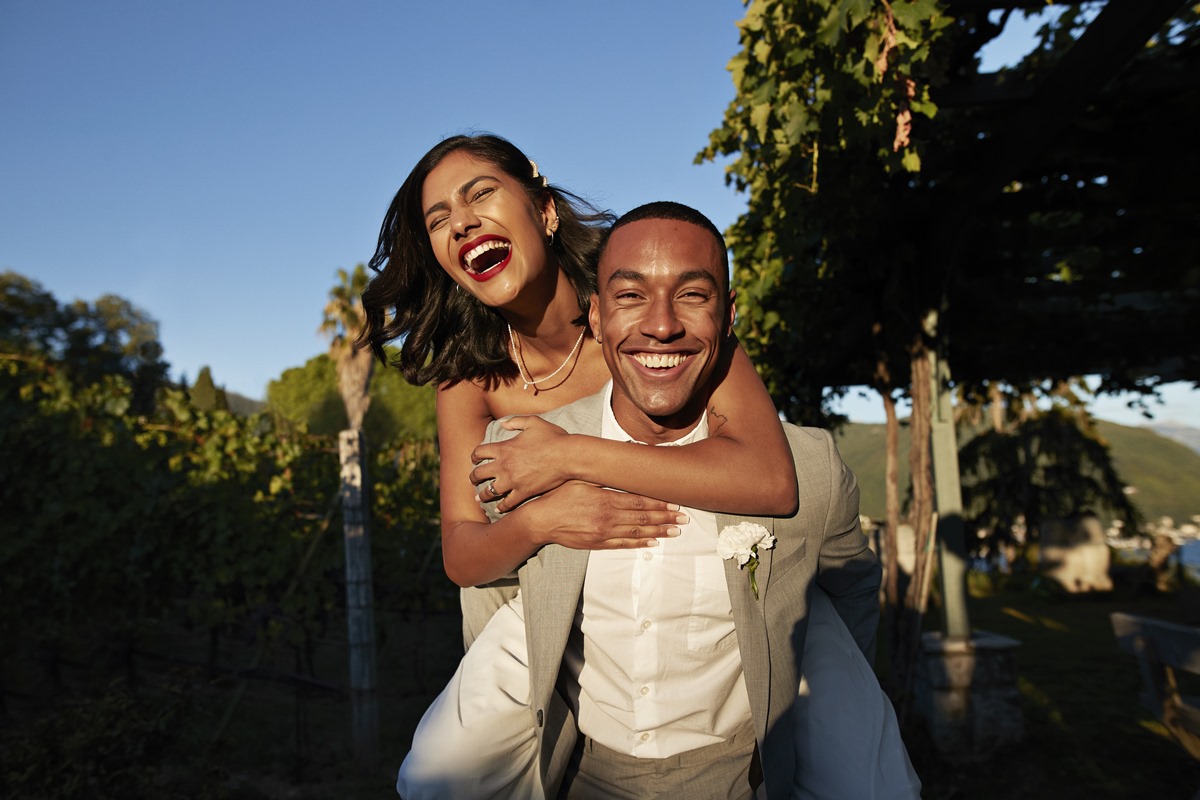 Foto colorida. Mulher está nas costas do homem. Eles estão sorrindo e muito felizes - Metrópoles