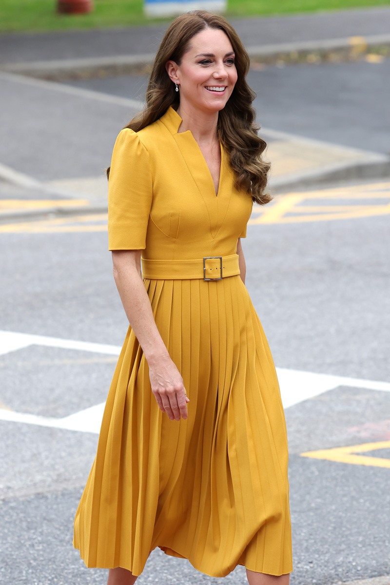 Foto colorida de mulher branca, com cabelo castanho e longo. Ela está andando e usa um vestido na cor amarelo - Metrópoles