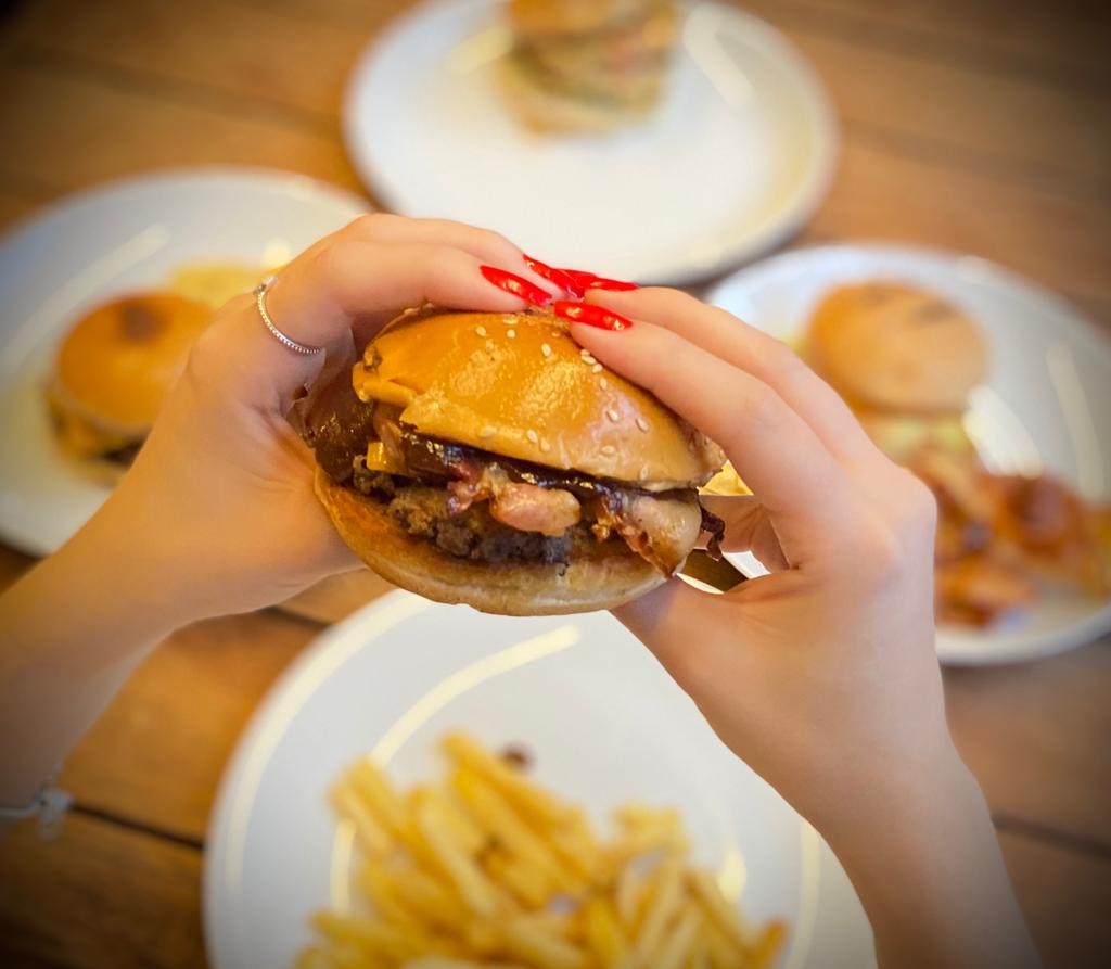 Na imagem, uma mão segura um delicioso hambúrguer de carne ladeado por batata frita - Metrópoles