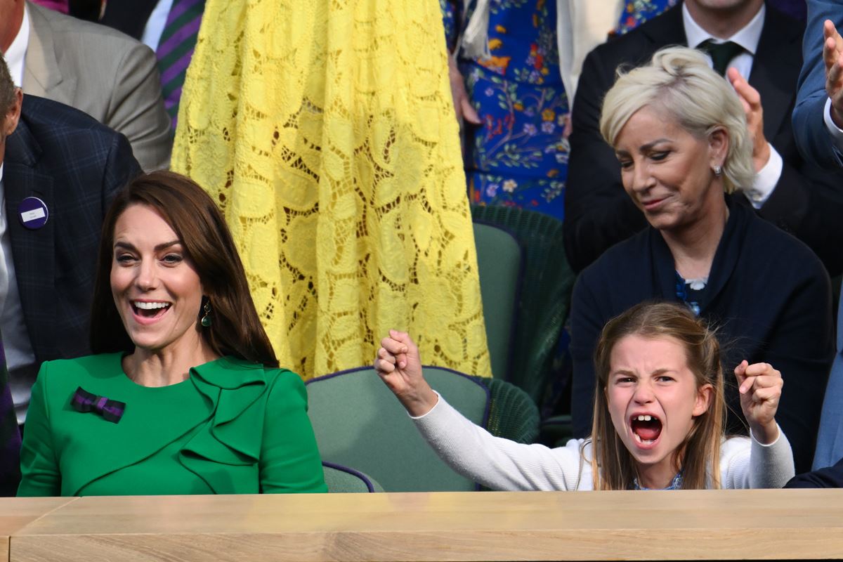 Foto colorida de mulher branca e com cabelo castanho ao lado de menina loira que está torcendo. Elas estão em uma arquibancada - Metrópoles