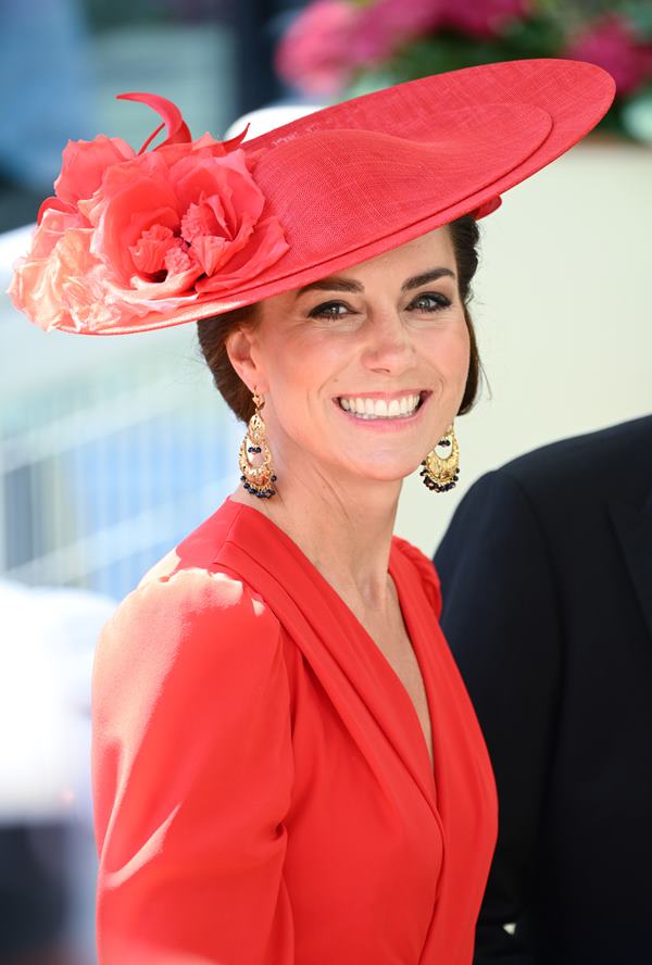 Mulher com chapéu vermelho. Ela está sorrindo, usando par de brincos dourados - Metrópoles