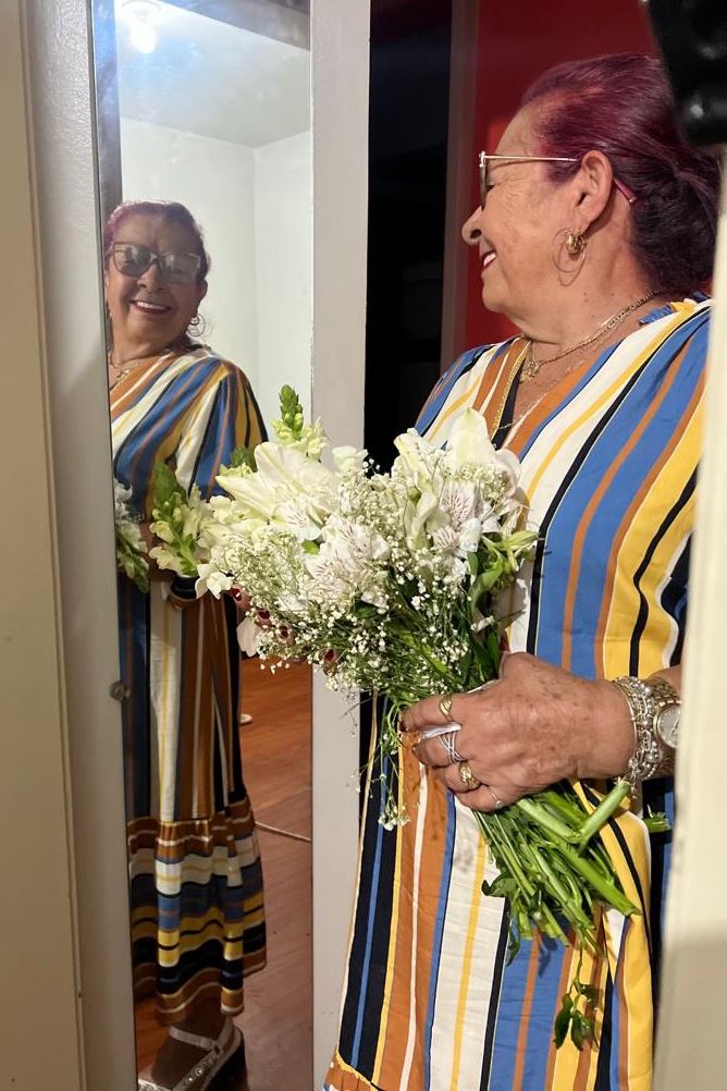 Foto de mulher diagnosticada com câncer de pulmão segurando buquê de flores brancas em frente a espelho - Metrópoles