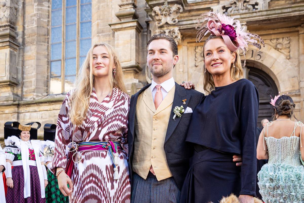 Foto colorida de um homem entre duas mulheres. Eles estão em frente a uma igreja e posando para foto - Metrópoles