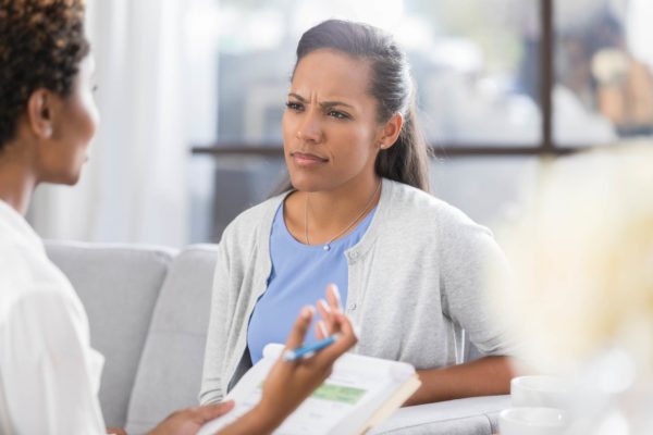 Paciente de aconselhamento adulto médio tem uma expressão confusa no rosto enquanto ouve um conselheiro. O conselheiro está gesticulando enquanto conversa com o paciente