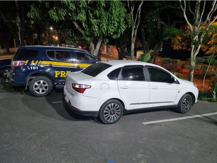 Em foto colorida carro branco ao lado de viatura da PRF em estacionamento - Metrópoles