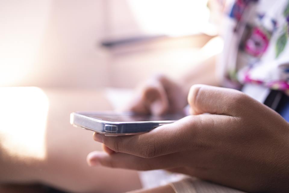 Foto colorida de uma mão de um adolescente usando smartphone no avião - Metrópoles