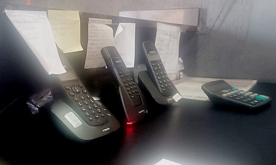 Em foto colorida três telefones pretos em balcão de comércio - Metrópoles