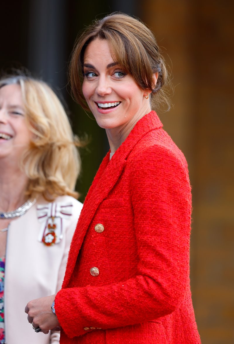 Foto colorida. Kate Middleton olha para o lado e sorri. Ela está com o cabelo amarrado em coque baixo dando destaque para sua franja - Metrópoles