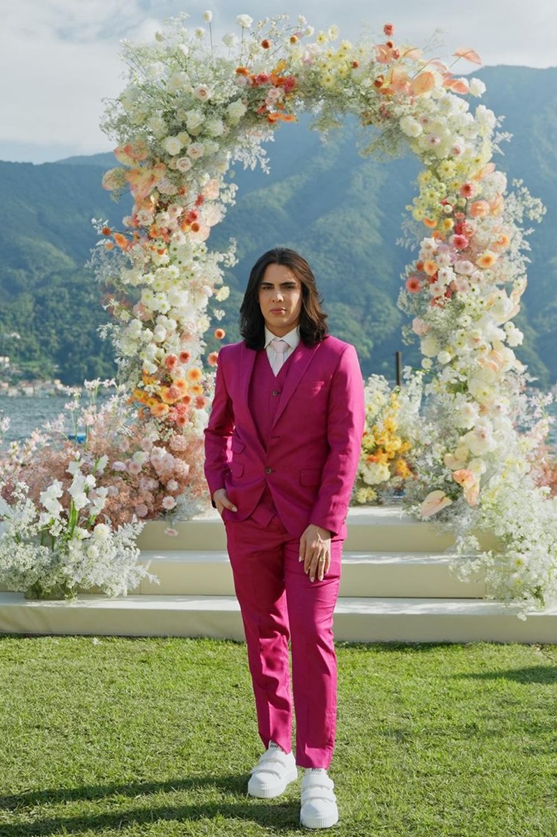 Foto colorida de homem pardo, de cabelo com tamanho médico e terno rosa. Ao fundo, há um arco florido - Metrópoles