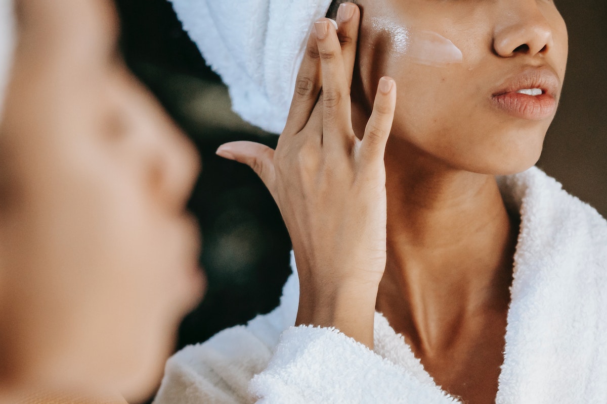 Jovem mulher negra aplicando creme em rosto - Metrópoles