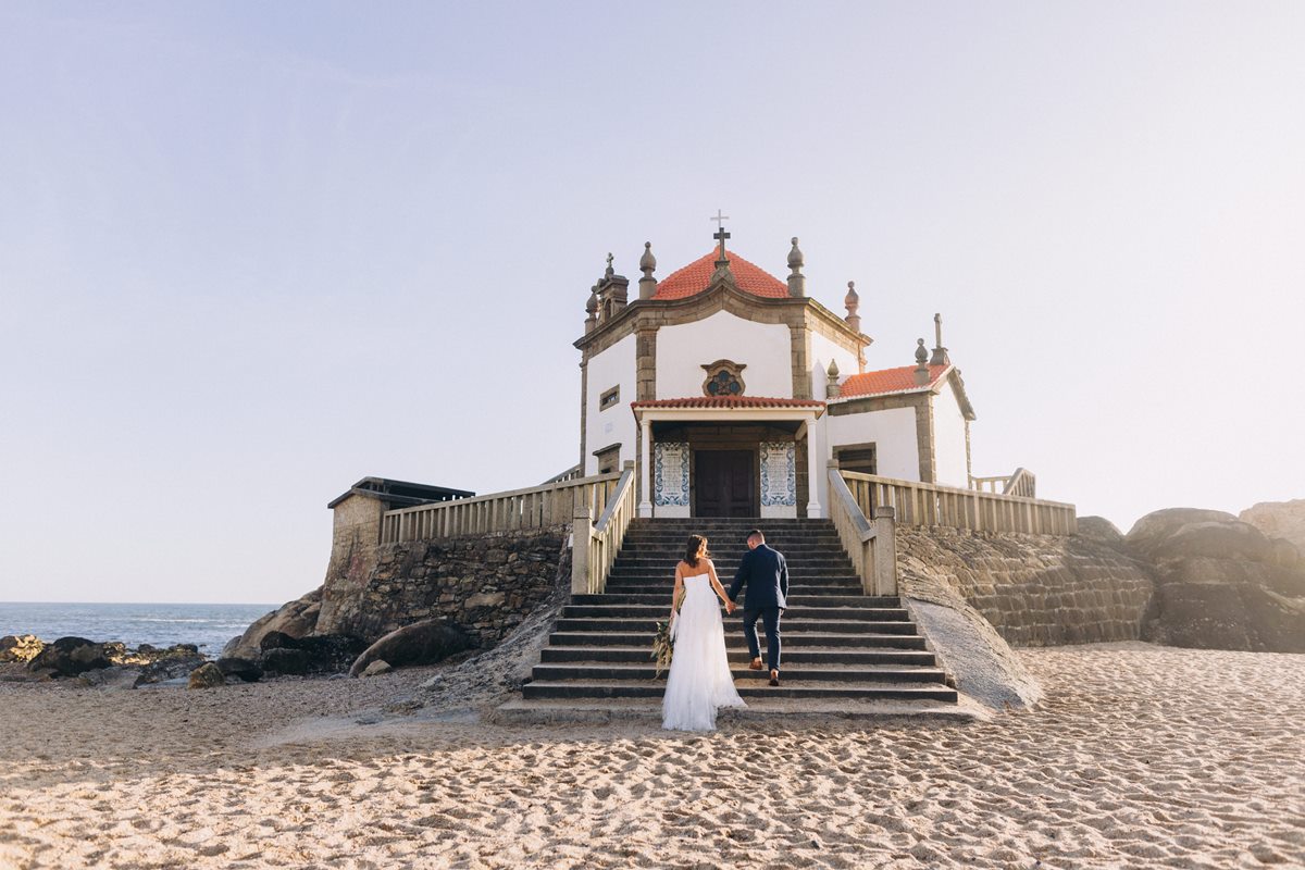 Foto colorida de casal de noivos subindo a escadaria de uma igreja - Metrópoles