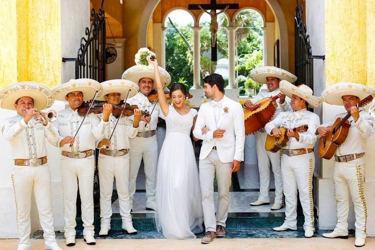 Foto colorida de noivos saindo de igreja enquanto grupo de música mexicana toca - Metrópoles