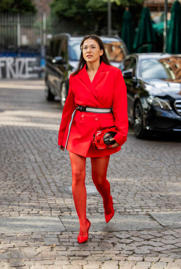 Na imagem com cor, uma mulher posando para foto com peças de roupa vermelhas - Metrópoles