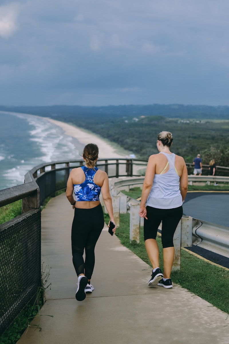 Duas mulheres de costas caminhando em calçada de frente para o mar - Metrópoles