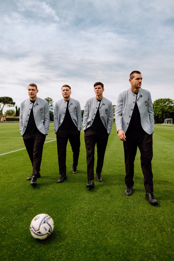 Quatro jogadores italianos de futebol andam sobre um gramado vestindo ternos - Metrópoles