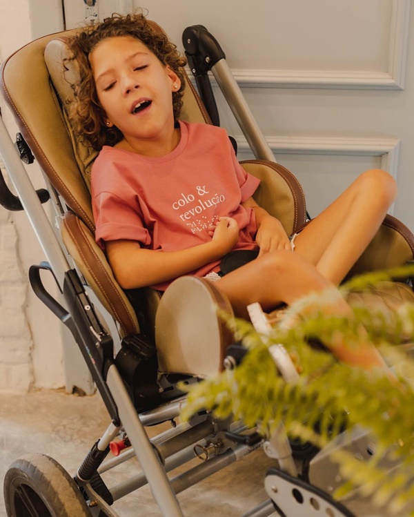 Foto colorida, de criança em carrinho de bebê e blusa laranja - Metrópoles