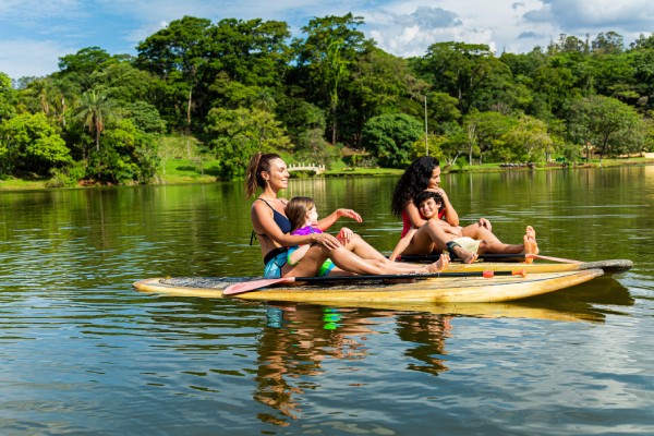 Fotografia colorida mostrando duas mães e filhos em cima de pranchas no meio de um lago-Metrópoles