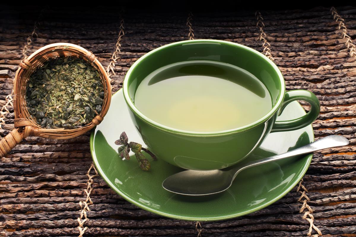 Foto colorida de chá verde em xícara de cor verde e ao lado, tem um pote com erva - Metrópoles