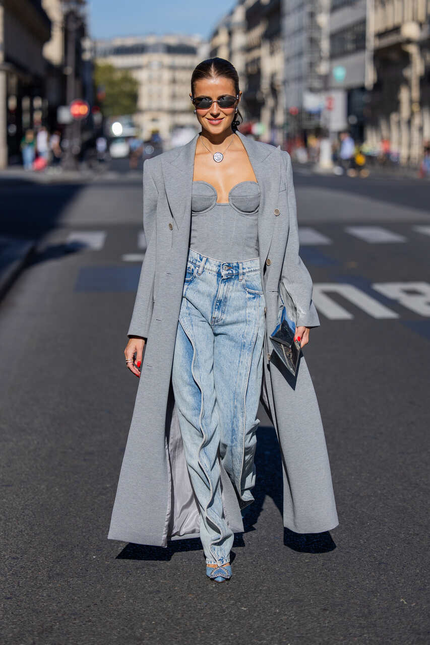 Na imagem com cor, uma mulher branca de cabelos presos posando para foto com um look todo cinza - Metrópoles