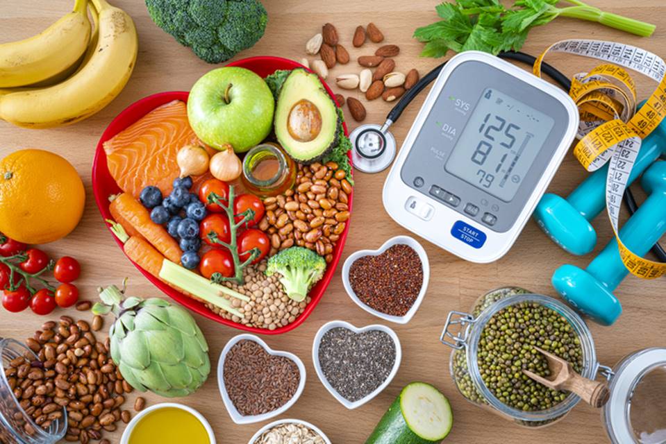 Foto de mesa com alimentos em recipientes em formato de coração e aparelho para medir a pressão - Metrópoles