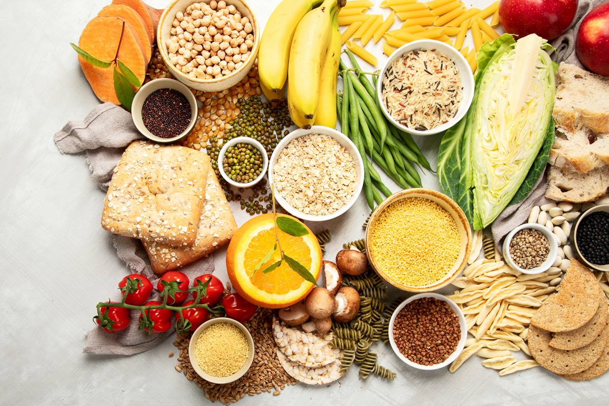 Foto colorida de pães, frutas, grãos e legumes, macarrão em uma mesa - Metrópoles