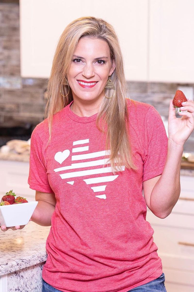 Foto colorida de mulher loira, com blusa rosa, segurando um morango e um pote com as frutas - Metrópoles