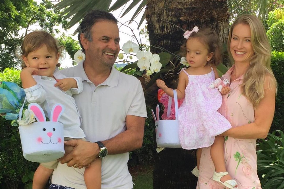 Foto colorida de homem segurando menino no colo, e mulher segurando menina no colo. As crianças estão com uma bolsa no formato de cabeça de coelho - Metrópoles