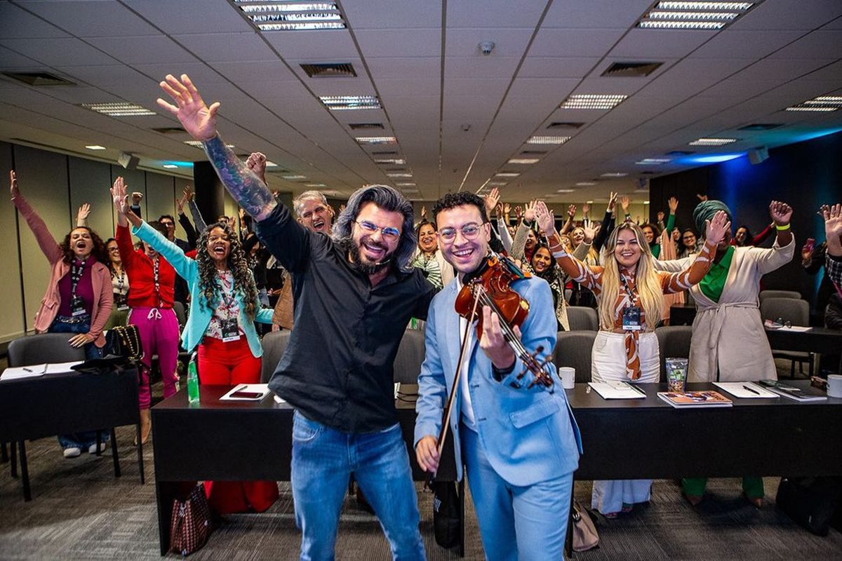 Foto colorida de pessoas com os braços levantados e um homem com um violino - Metrópoles